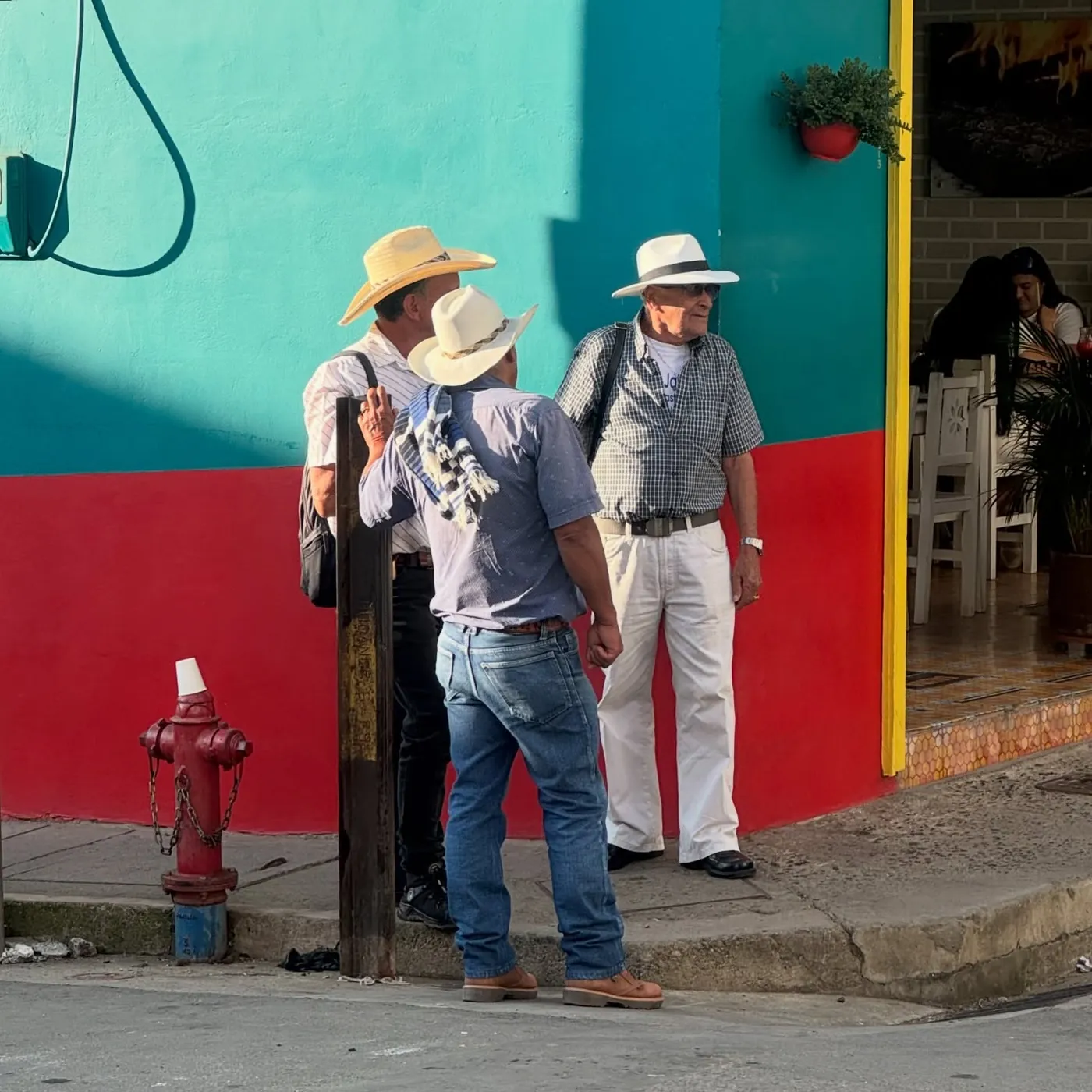 Men in hats in front of a turquoise and red wall, Jardín