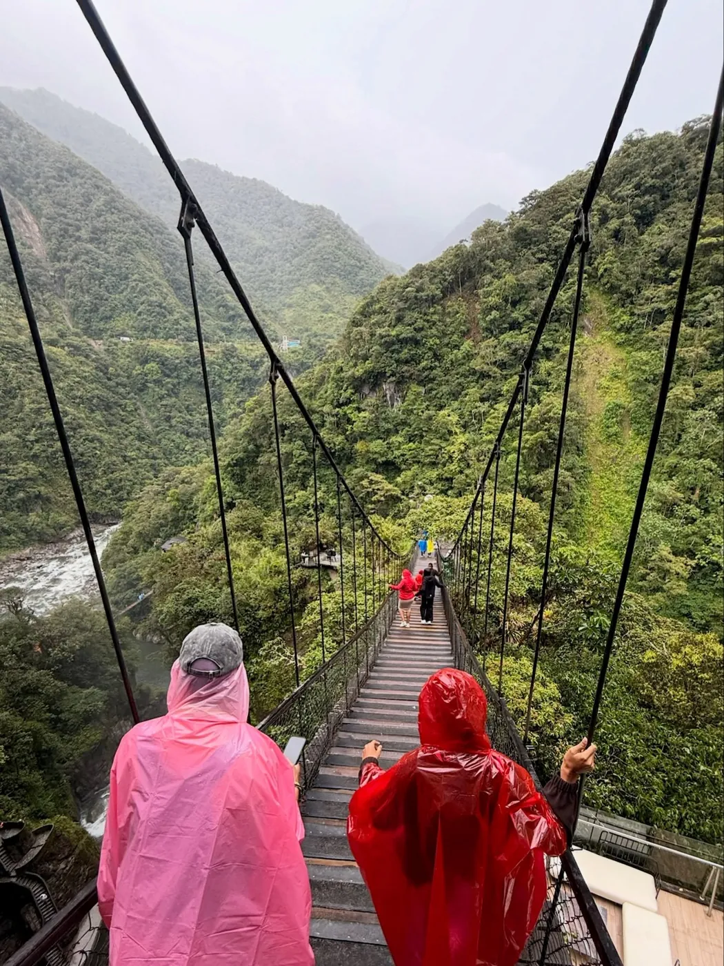 Friends in pink and red ponchos on a hanging bridge, Baños
