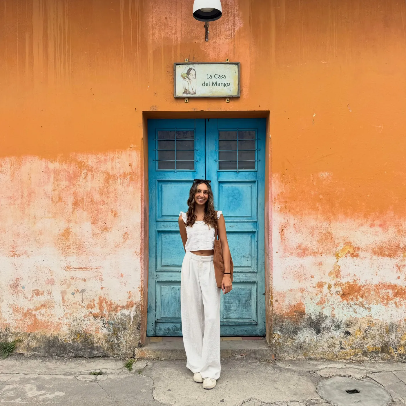 Natasha in white in front of an orange wall and a blue door in Antigua